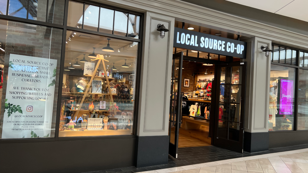 The storefront of Local Source Co-Op at the Westfield Fashion Square mall, featuring a window display of local artisan goods and the official shop entrance.